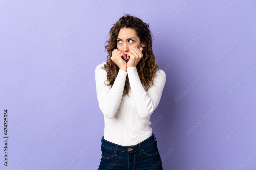Young caucasian woman isolated on purple background nervous and scared putting hands to mouth