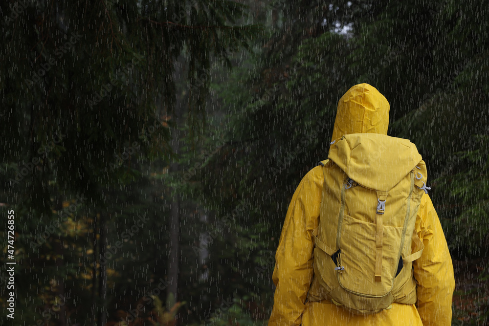 Woman with raincoat and backpack in forest under rain, back view Woman with raincoat and backpack in forest under rain, back view