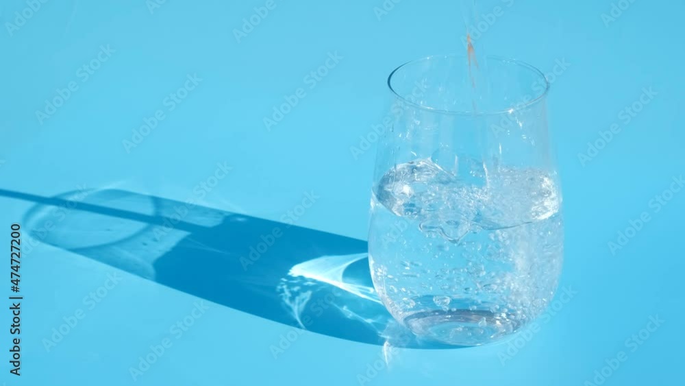 Water is poured into a glass on blue background, close up. Water is poured into a glass on blue background, close up.