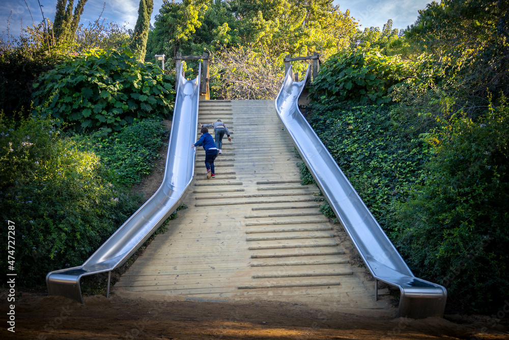 Φωτογραφία Two kids, a girl and a boy in a playground going up the stairs to go down the sl