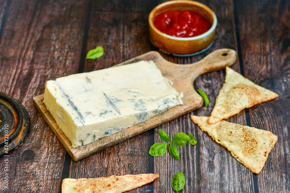 Gorgonzola cheese on cutting board with fresh basil and home made crispy nachos with spicy red sauce. Veined Italian blue cheese. Gorgonzola cheese on cutting board with fresh basil and home made crispy nachos with spicy red sauce. Veined Italian blue cheese.