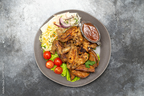 Griled chiken wings with tomatoes and green letuce salad, cabbage salad and red onion, grilled potatoes on the plate.