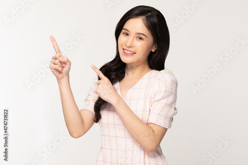 Happy attractive asian young woman smile and pointing to copy space isolated on white background.Cheerful pretty girl wear casual dress pointing finger to empty space for mockup to display product