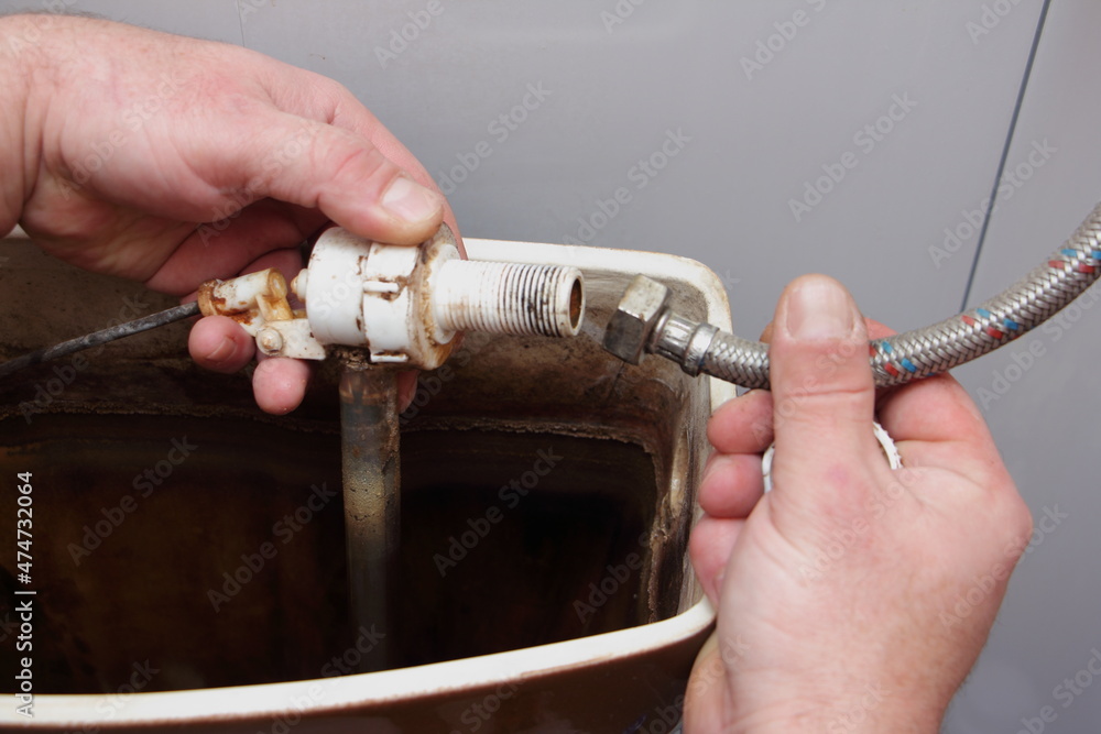 The plumber's hands remove the old dirty water fill valve from filling