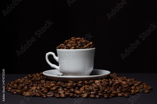 Coffee beans on a black background. A coffee cup full of coffee beans. Large serving of caffeine
