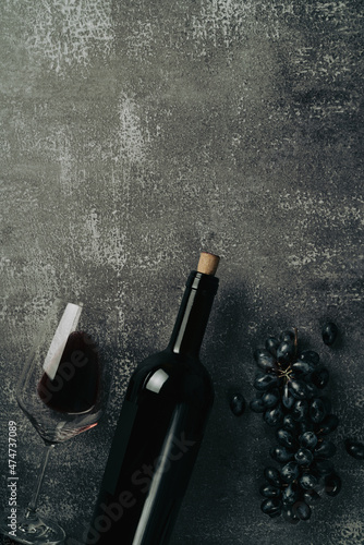 Glass of red wine,black grape and lying bottle on black stone desk. Top view with copy space.