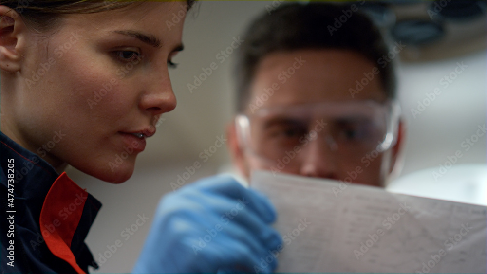 Fototapeta premium Portrait of serious paramedics looking at electrocardiogram graphs on paper