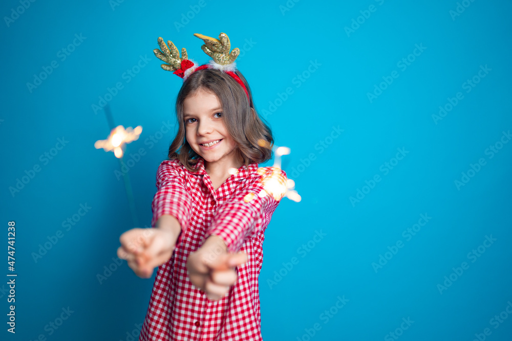 Happy small girl looking with admiration at burning sparkler in her hand over blue background Happy small girl looking with admiration at burning sparkler in her hand over blue background