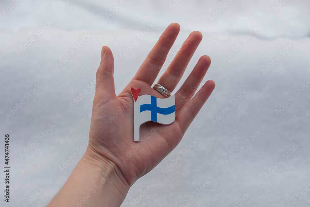 Finland flag in hand on snow. Travel to Finland concept. Trip to Helsinki in miniature. Finland national holiday idea. Nordic country symbol. Finland flag in hand on snow. Travel to Finland concept. Trip to Helsinki in miniature. Finland national holiday idea. Nordic country symbol.