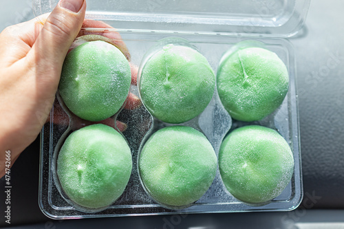 Macro closeup of hand holding storebought frozen ice cream filled mochi rice cake Japanese dessert with green tea matcha flavor showing texture photo