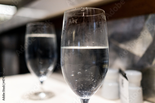 Macro closeup of two glasses glass with water on restaurant table for dinner with bokeh background in dark room atmosphere