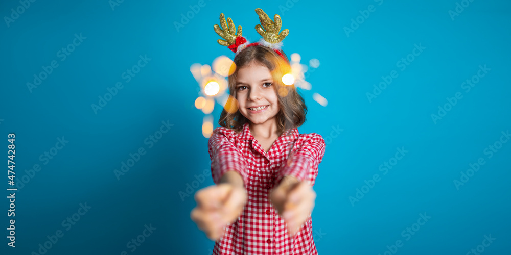 Happy small girl looking with admiration at burning sparkler in her hand over blue background Happy small girl looking with admiration at burning sparkler in her hand over blue background