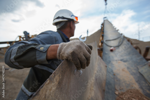 Extraction of gold ore. Mining and processing plant. Rubber conveyor belt. Worker hold wrench tool, hand in focus. Other is blurred. No face,white hardhat,orange glasses. Almaty reg.,Kazakhstan.