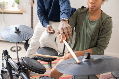 African male teacher explaining biracial schoolgirl with drumsticks how to play drumkit at home lesson