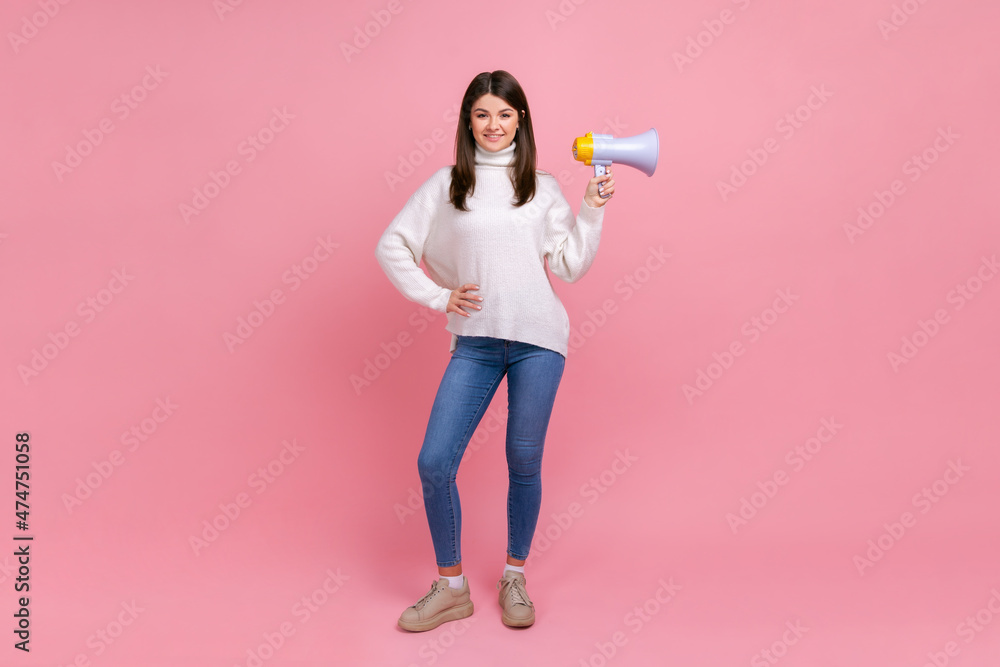 Full length portrait of good looking confident female standing with megaphone, keeping hand on hip, wearing white casual style sweater. Indoor studio shot isolated on pink background. Full length portrait of good looking confident female standing with megaphone, keeping hand on hip, wearing white casual style sweater. Indoor studio shot isolated on pink background.