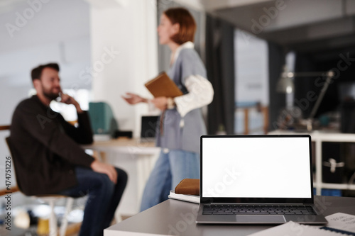 Close-up of workpalce of business person with laptop on it for online work at office with business people in the background