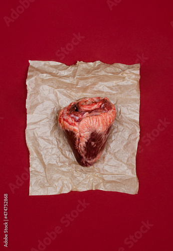 Top view of real animal heart on a piece of craft paper and red background.