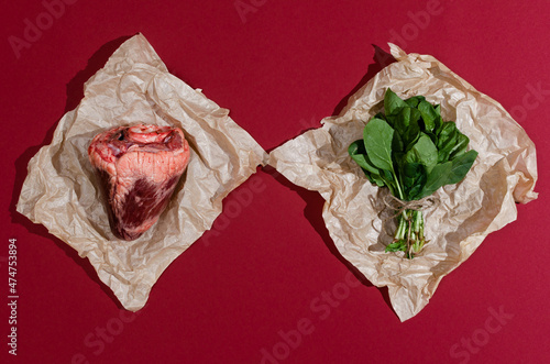 Creative flat lay of a real animal heart meat and spinach on craft paper and red burgundy background. photo