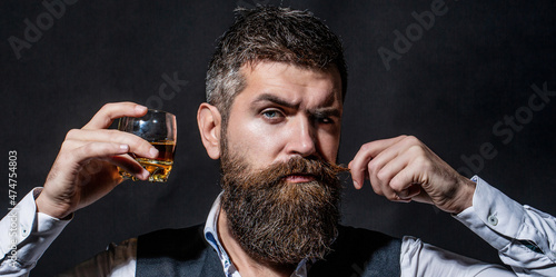 Man with beard holds glass of brandy. Tasting and degustation concept. Bearded businessman in elegant suit with glass of whiskey. Man drinking whiskey, brandy, cognac. Degustation, tasting