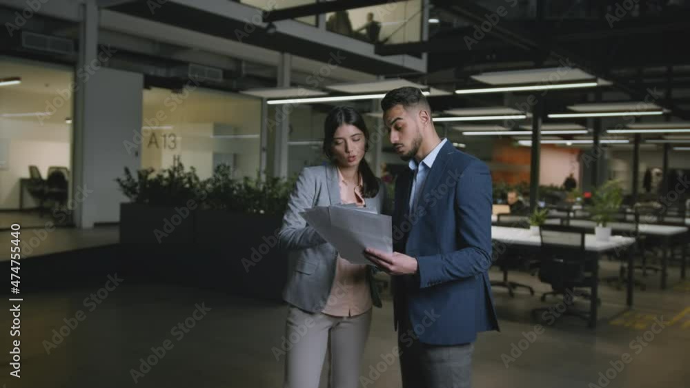 Young confident caucasian woman and arab man coworkers discussing business documents at modern office, tracking shot Young confident caucasian woman and arab man coworkers discussing business documents at modern office, tracking shot