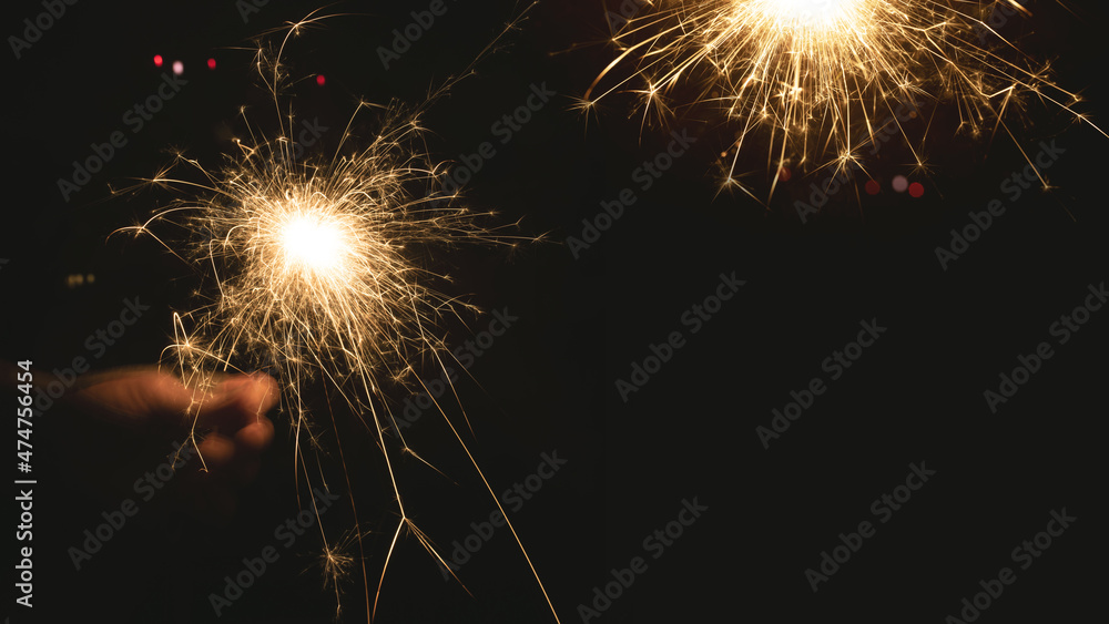 Burning sparkler at night. Hand holds a burning sparkler at night. Christmas background with colorful bokeh and space for text.