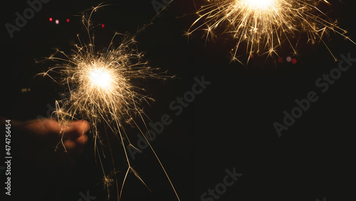 Burning sparkler at night. Hand holds a burning sparkler at night. Christmas background with colorful bokeh and space for text.