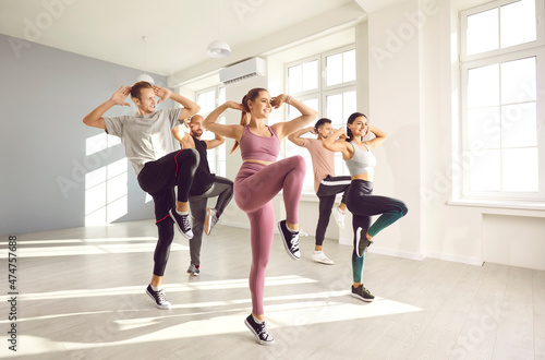 Fototapeta Naklejka Na Ścianę i Meble -  Group of young people in sportswear enjoying an active aerobics class with a professional fitness trainer. Team of motivated friends who want to stay in good shape doing a cardio workout at the gym