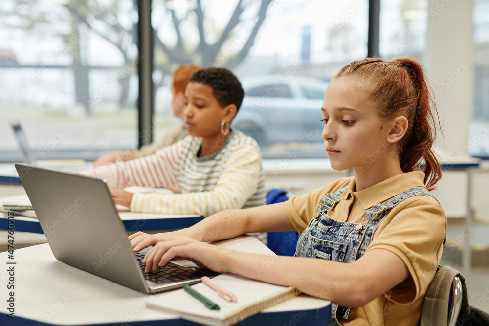 Side view portrait of diverse group of children in row using laptops in coding class, copy space Side view portrait of diverse group of children in row using laptops in coding class, copy space