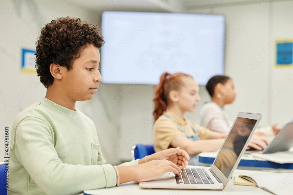Side view portrait of teenage boy using laptop in coding class for children, copy space Side view portrait of teenage boy using laptop in coding class for children, copy space