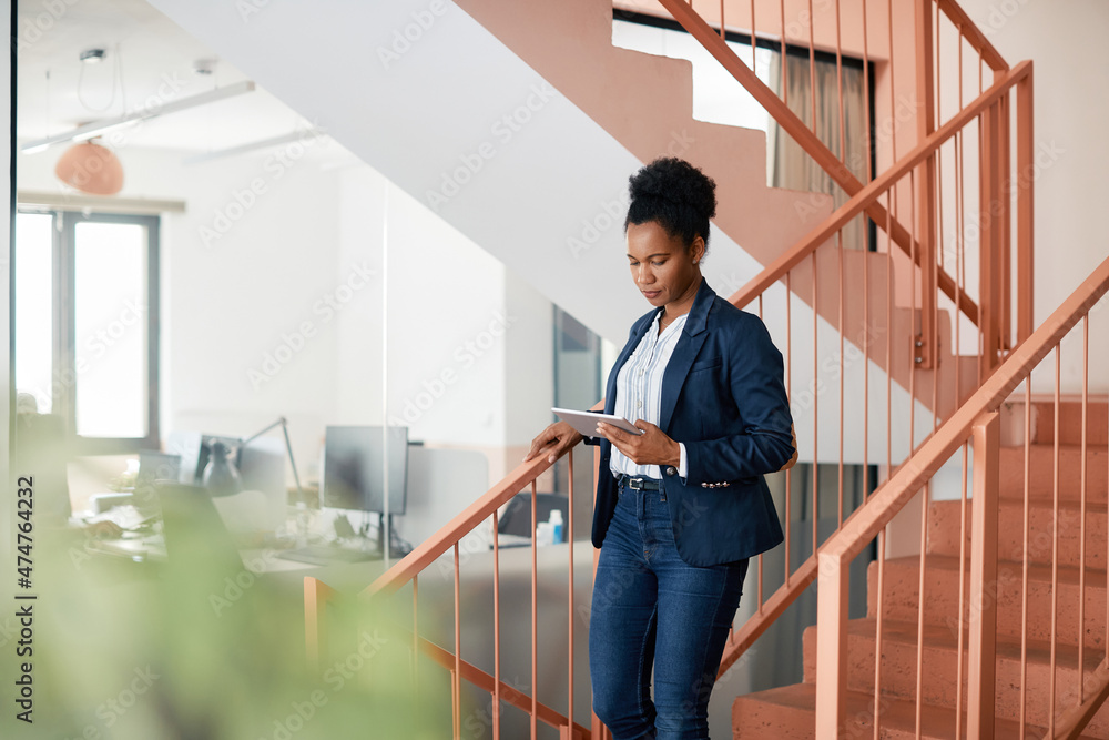 Black businesswoman uses digital tablet while walking down the stairs. Black businesswoman uses digital tablet while walking down the stairs.
