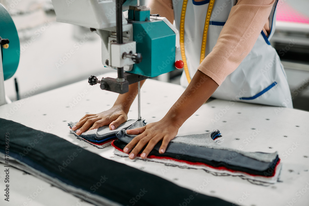 Close-up of textile worker cuts fabric with machine in factory.