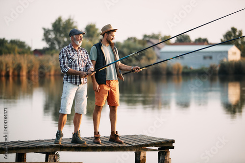 Full length of senior man and his son freshwater fishing from pier.