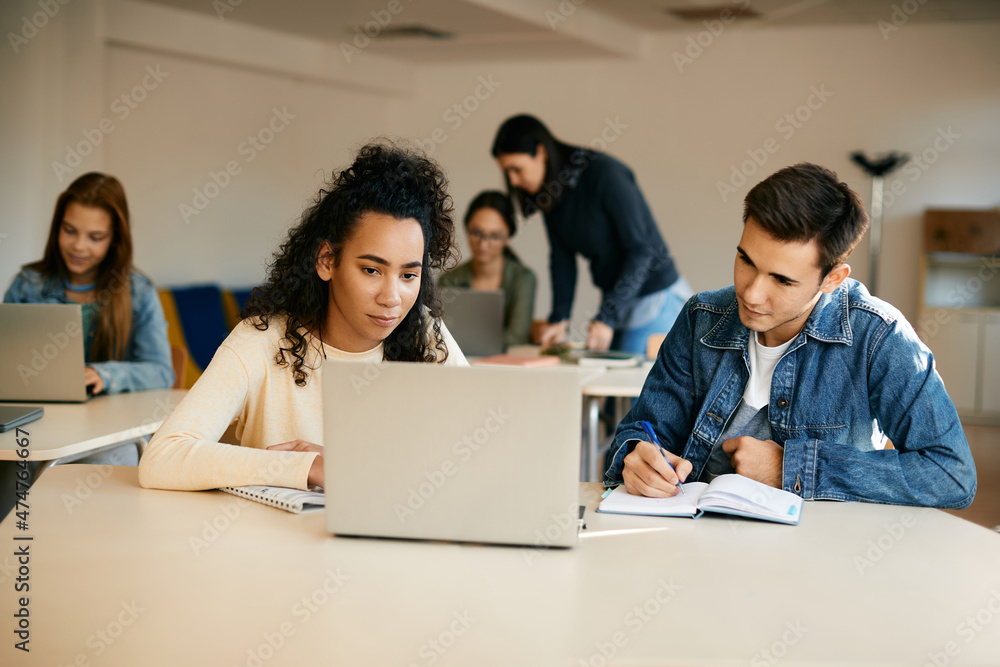 © Drazen - High school classmates take notes while e-learning on laptop in classroom.