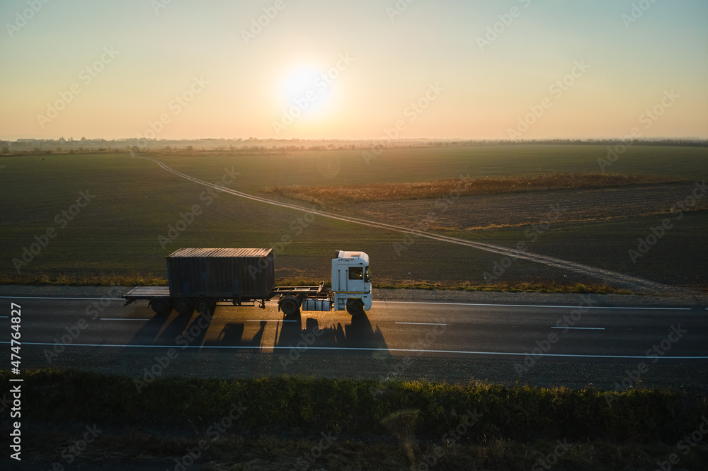 Fototapeta premium Aerial view of blurred fast moving semi-truck with cargo trailer driving on highway hauling goods in evening. Delivery transportation and logistics concept