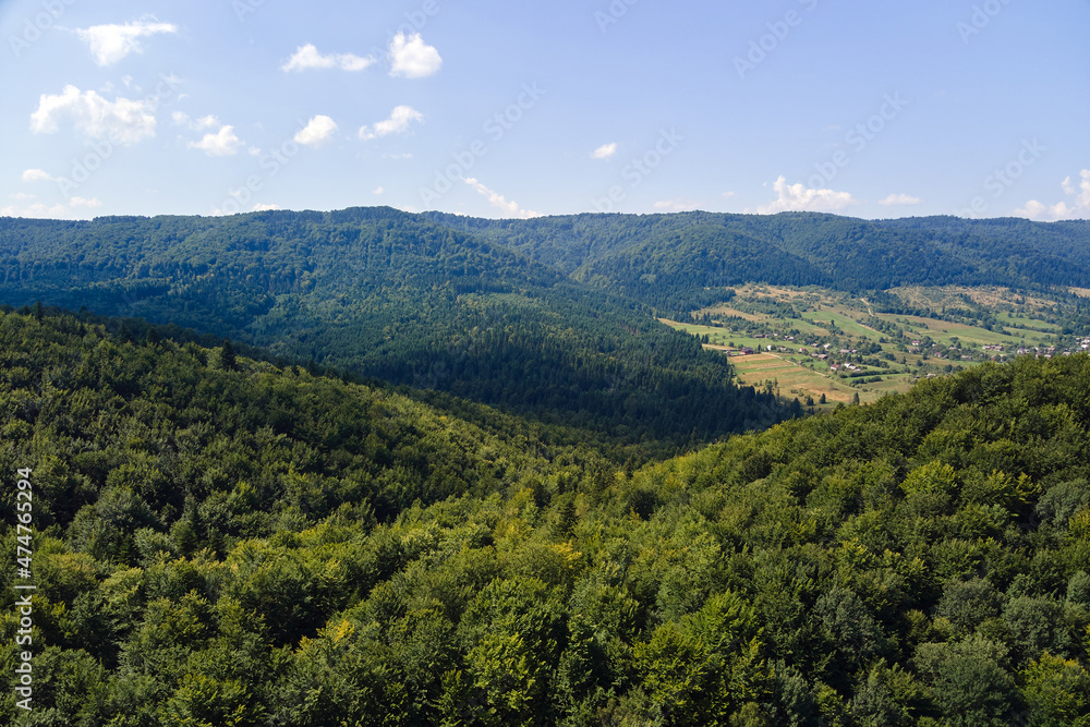 Aerial view of mountain hills covered with dense green lush woods on bright summer day