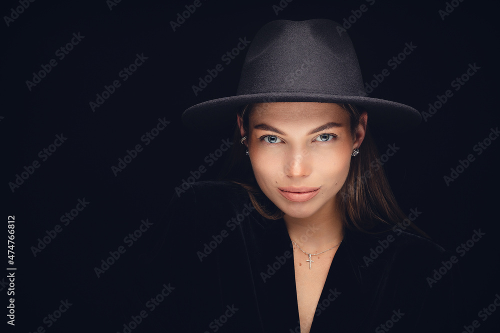 Fashionable studio portrait of a beautiful young girl in black hat on a black background. Low key. Fashionable studio portrait of a beautiful young girl in black hat on a black background. Low key.