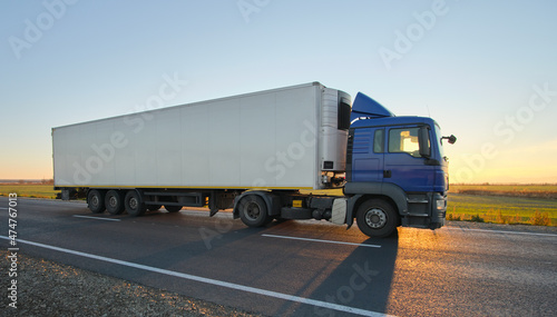 Semi-truck with cargo trailer driving on highway hauling goods in evening. Delivery transportation and logistics concept