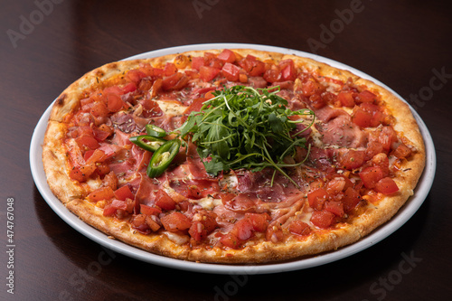 ham pizza with tomatoes, cheese and topped with green chili peppers and arugula