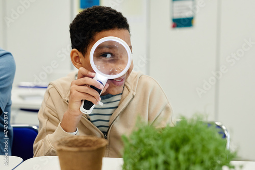 Portrait of teenage kid playing with magnifying glass in school