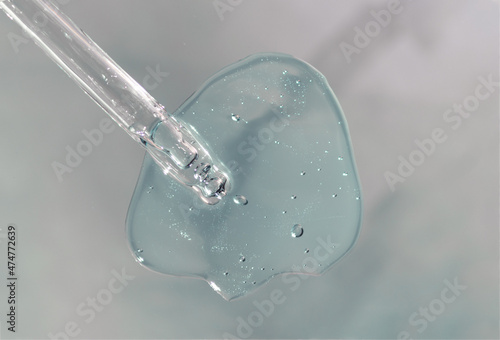 Pipette with fluid hyaluronic acid on gray background. Cosmetics and healthcare concept closeup. Dose of serum or retinol with air bubbles. Flat lay. Luxury gel or beauty product presentation in macro © Lavsketch