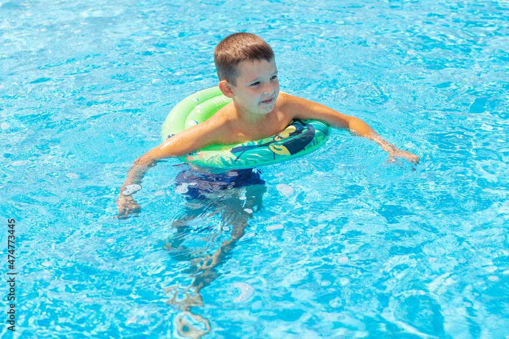 Funny happy child boy in swiming pool on inflatable rubber circle ring. Kid playing in pool. Summer holidays and vacation concept
