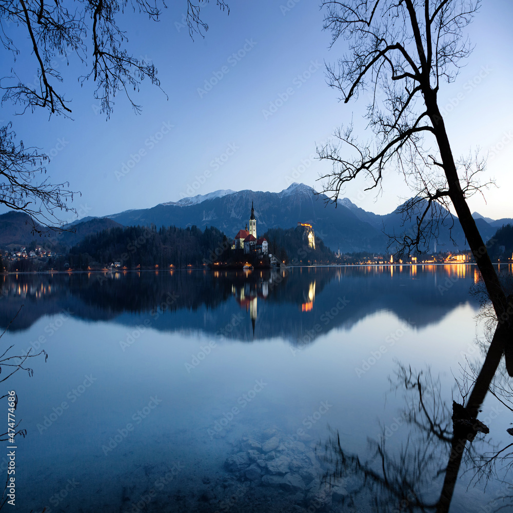 A morning landscape with a lake, an island, a castle and mountains. Lake Bled, Slovenia, blue hour. Square landscape. Postcard view with reflection of mountains in lake.