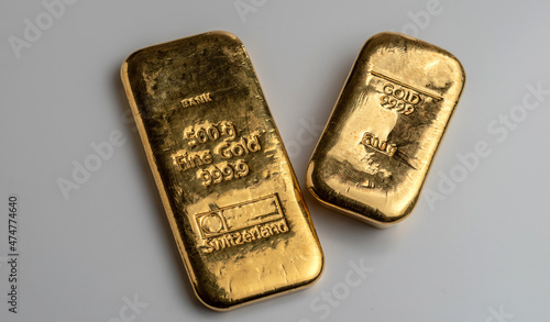 Two gold bars from different manufacturers weighing 500 grams each on a grey background.