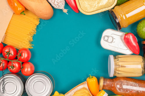 Food bank, food delivery concept. Frame made of food donations on green background with copy space - pasta, fresh vegatables, canned food, baguette and other groceries