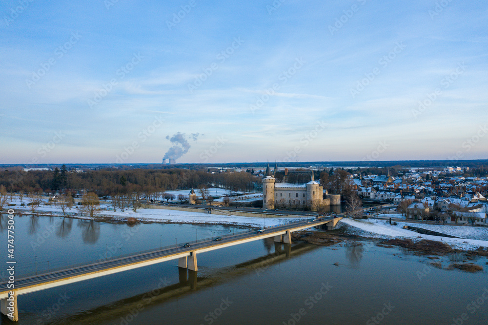 The Sully sur Loire bridge and its town center under the snow in Europe, in France, in the Center region, in the Loiret, towards Orleans, in Winter, on a sunny day.