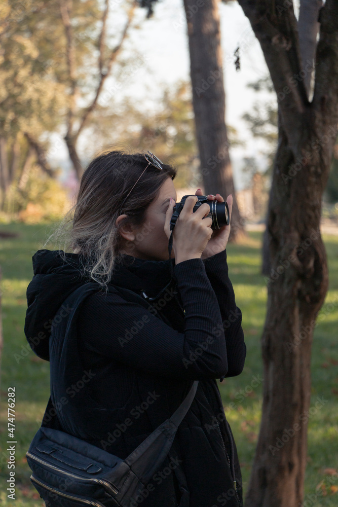 Female photographer, taking pictures with her digital camera of forest landscape at sunset. A girl in black is taking photograph in forest. Green background. Unrecognizable person. Female photographer, taking pictures with her digital camera of forest landscape at sunset. A girl in black is taking photograph in forest. Green background. Unrecognizable person.