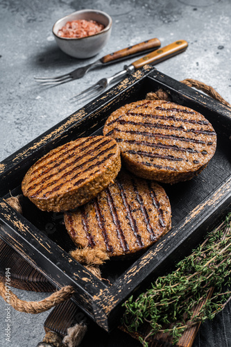 Roasted meat free patties, plant based meat burger cutlets in wooden tray with herbs. Gray background. Top view