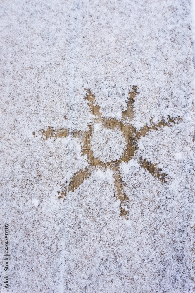 Drawing of the sun on a wooden sidewalk covered with snow. Sun on a white background. Drawing of the sun on a wooden sidewalk covered with snow. Sun on a white background.