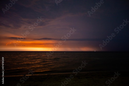 Lightning bolts illuminate the sky at night in the sea © Hennadii