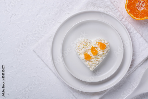 Heart shaped cottage cheese and orange in a plate on a white table.